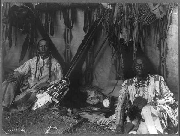 Image: Photograph of Little Plume and son Yellow Kidney sitting in a lodge. Taken by Edward Curtis in 1910. From the Library of Congress.